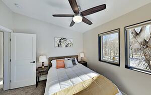 Guest room with queen bed, ceiling fan, and windows
